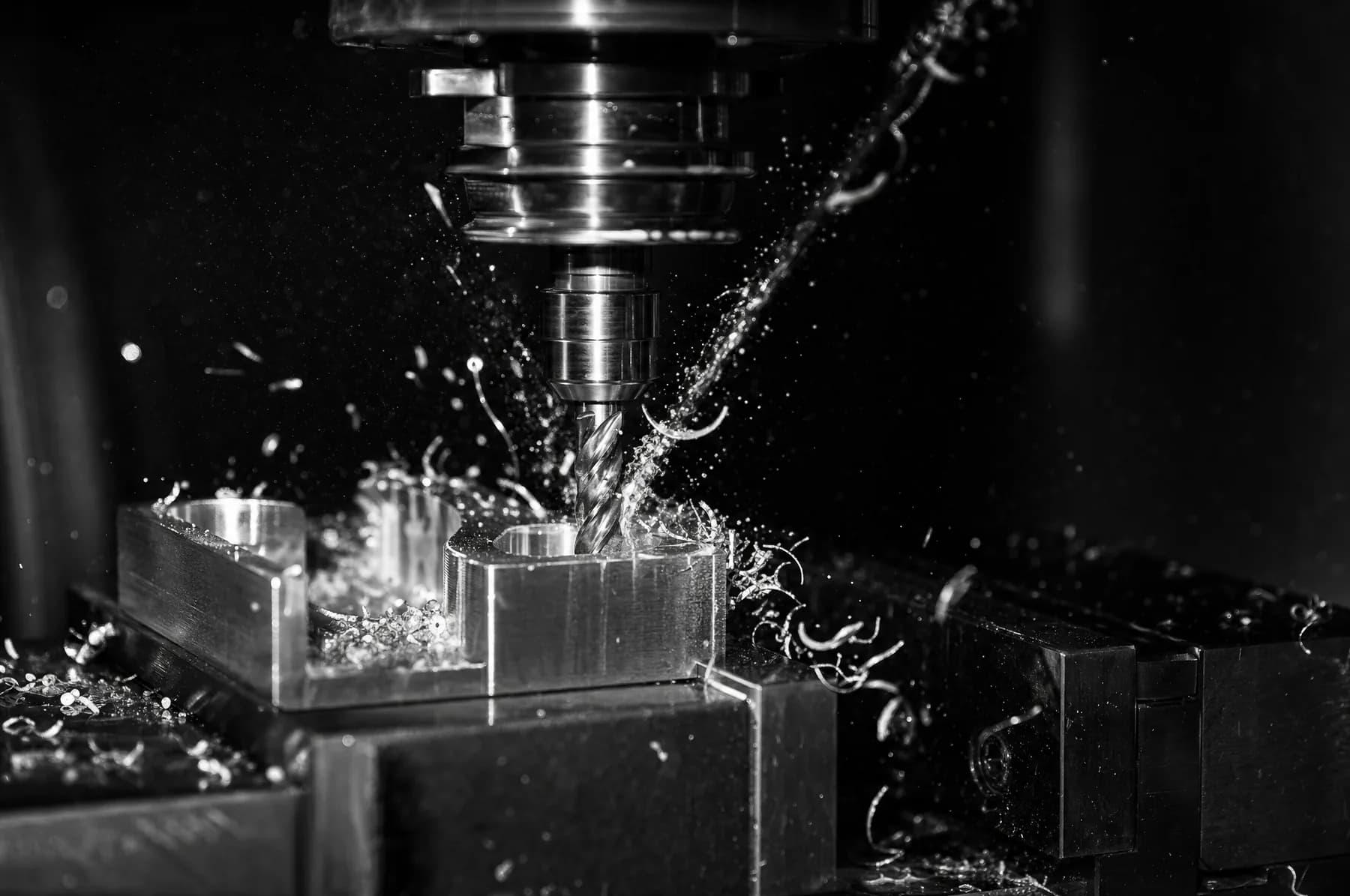 An end mill cutting an aluminium block with coolant spraying off the tool and chips curling away