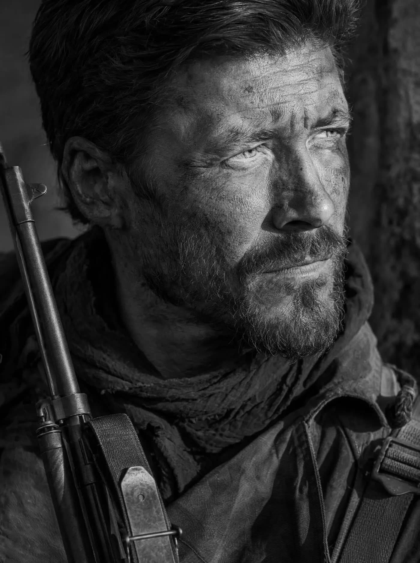 A weathered man with a slung rifle, photographed close in hard side light
